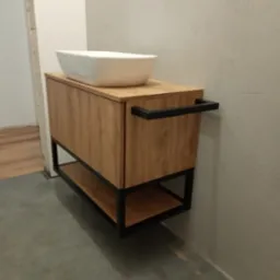 Nowoczesna szafka łazienkowa z blatem z imitacji drewna i czarną metalową ramą, na której stoi biała umywalka nablatowa o kwadratowym kształcie.