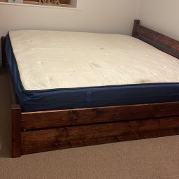 Marcin Konkol - Łóżko z ciemnego drewna z materacem w pokoju z oknem, na parapecie dekoracja 'Relax'