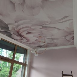 Remontuj Zbigniew Zając - Różowe kwiaty na suficie w pokoju z oknem, grzejnikiem i drabiną, oświetlone dekoracyjną lampą