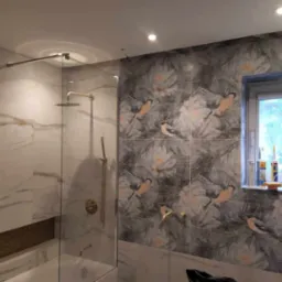 Nowoczesna łazienka z kabiną prysznicową typu walk-in, marmurowymi płytkami na ścianie i dekoracyjnymi płytkami z motywem kwiatowo-ptasim na sąsiedniej ścianie, widoczne akcesoria łazienkowe...