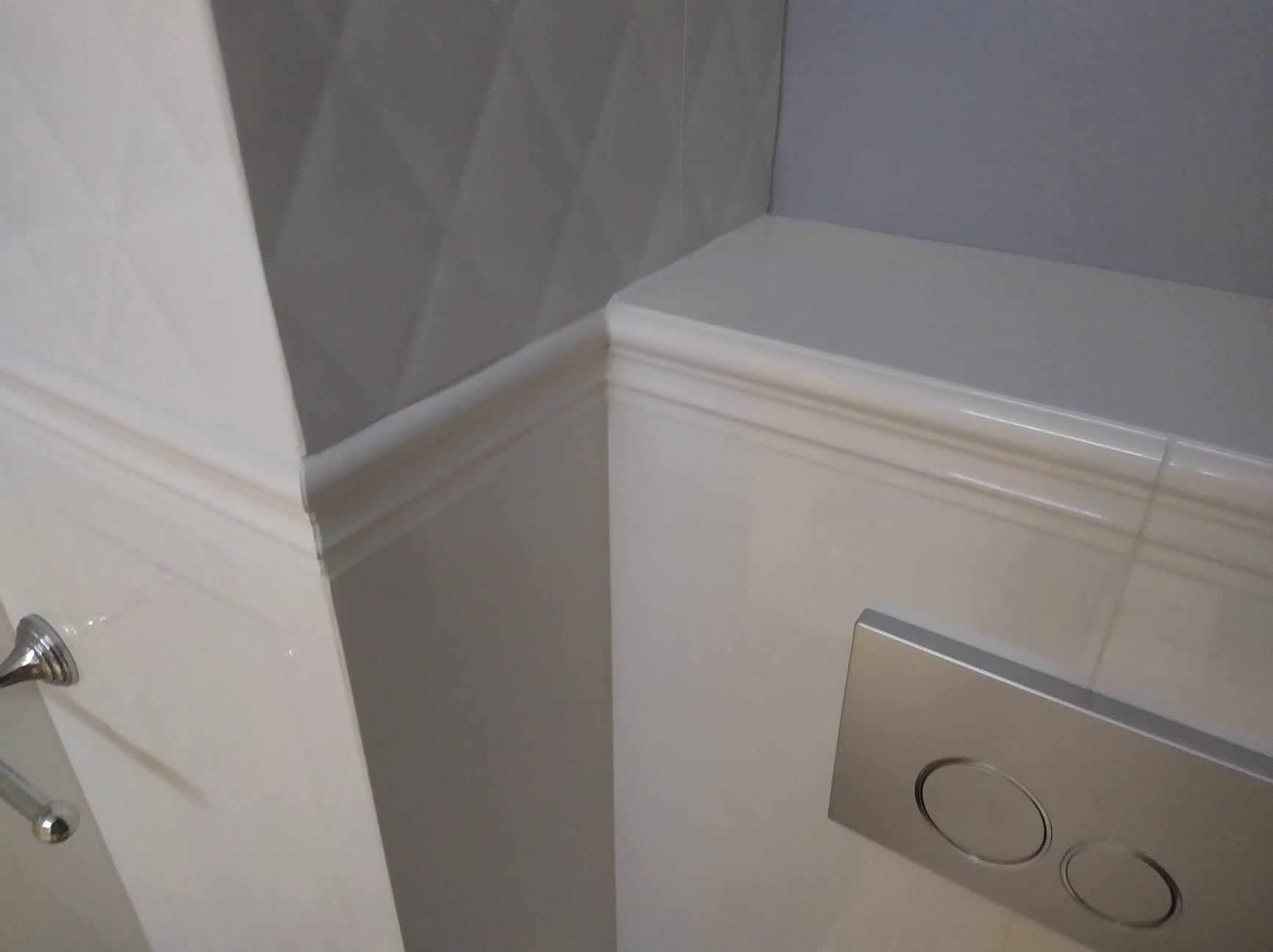 Wykończona łazienka z białymi płytkami imitującymi boazerię i srebrnym przyciskiem spłuczki