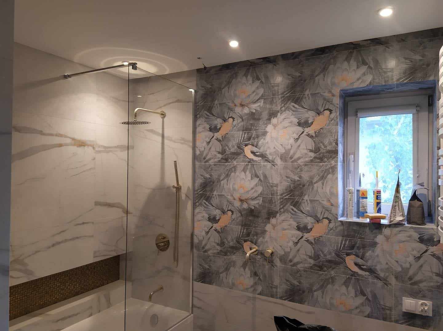 Nowoczesna łazienka z kabiną prysznicową typu walk-in, marmurowymi płytkami na ścianie i dekoracyjnymi płytkami z motywem kwiatowo-ptasim na sąsiedniej ścianie, widoczne akcesoria łazienkowe...