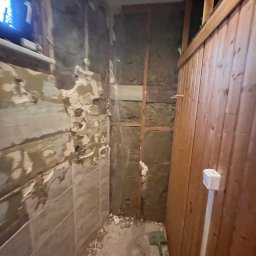 Usługi budowlane - Demontaż starej glazury w łazience w Żarach. Widoczne odsłonięte ściany, fragmenty płytek i instalacji. Przygotowanie do dalszych prac wykończeniowych.