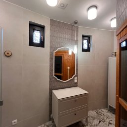 Usługi budowlane - Jasna łazienka po remoncie: beżowe płytki, marmurowa podłoga, szafka z lustrem i czarne okna. Minimalistyczny design z akcentami drewna.