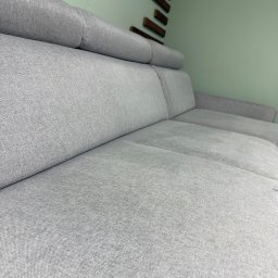 Czysta tapicera - Szczegółowe ujęcie szarej, modułowej sofy z zagłówkami na tle pistacjowej ściany z drewnianą dekoracją. Widoczna faktura tkaniny i precyzyjne szwy.