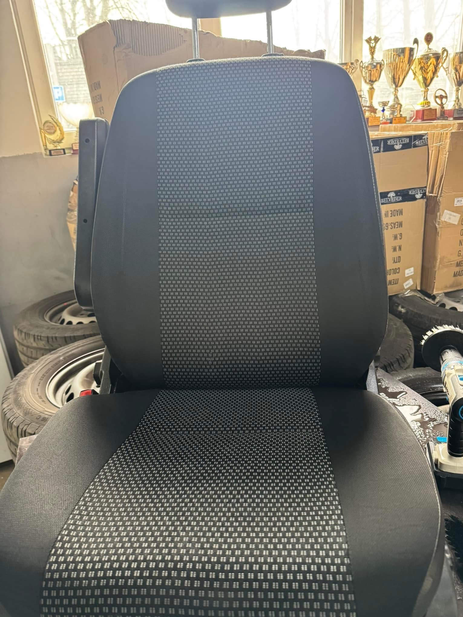 Wyczyszczone, szare siedzenie samochodowe z wzorem w kropki, na tle opon i pudeł. Widoczne ślady wilgoci po czyszczeniu.