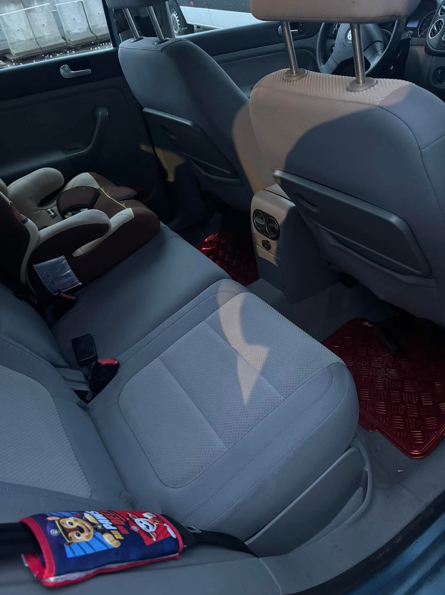Wnętrze samochodu z szarą tapicerką, fotelikiem dziecięcym i czerwonymi dywanikami. Widoczne zabrudzenia na siedzeniu.