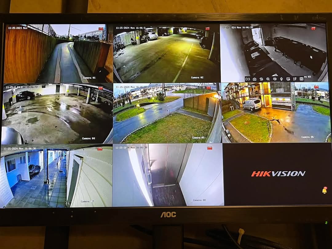 Ekran monitora z podglądem z kilku kamer monitoringu, widoczne różne ujęcia parkingów, wjazdów i budynków, logo Hikvision w prawym dolnym rogu.