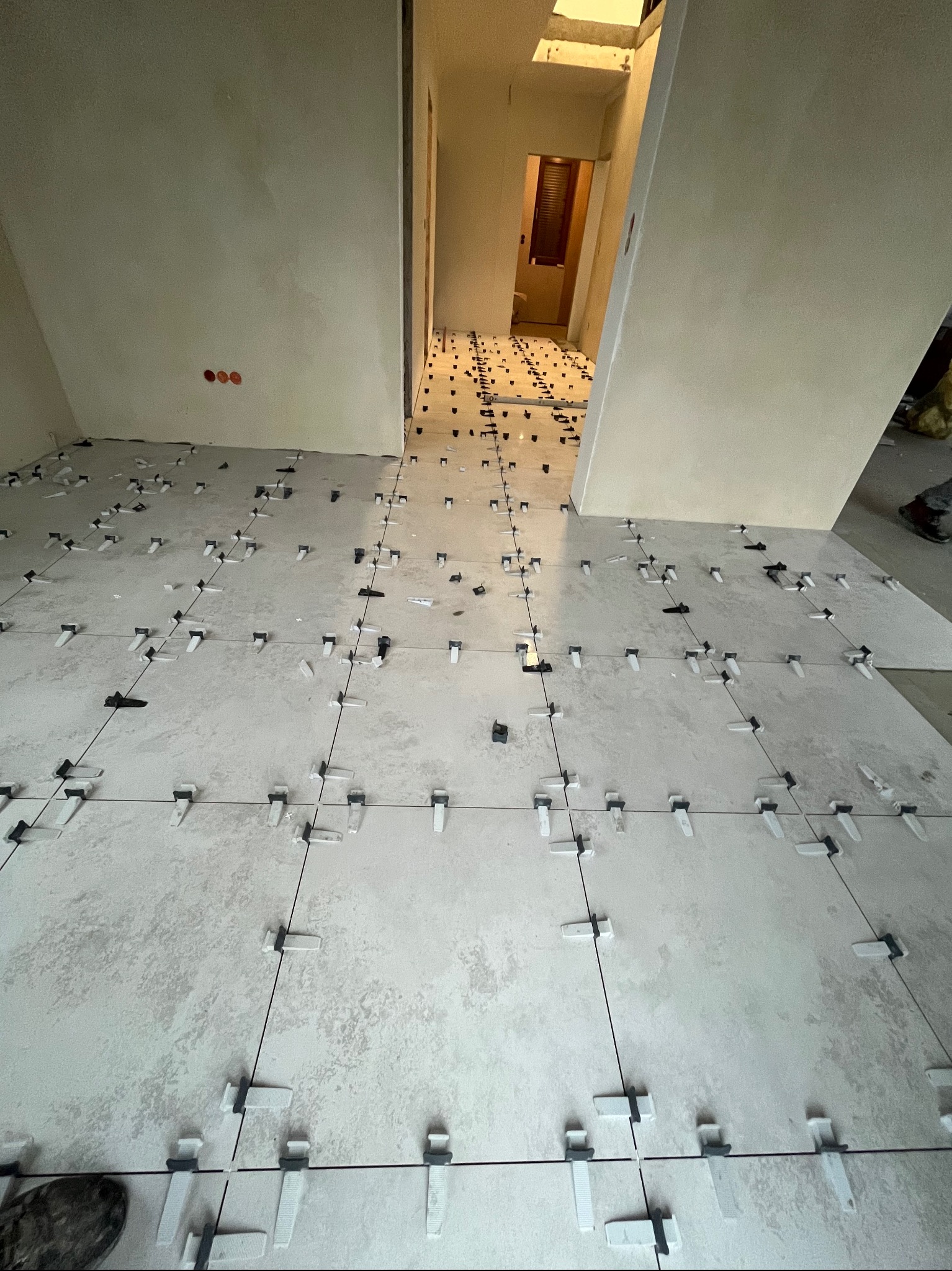 Układanie jasnych, kwadratowych płytek podłogowych z użyciem klipsów poziomujących, widok z góry na posadzkę w trakcie prac wykończeniowych w nowym mieszkaniu.