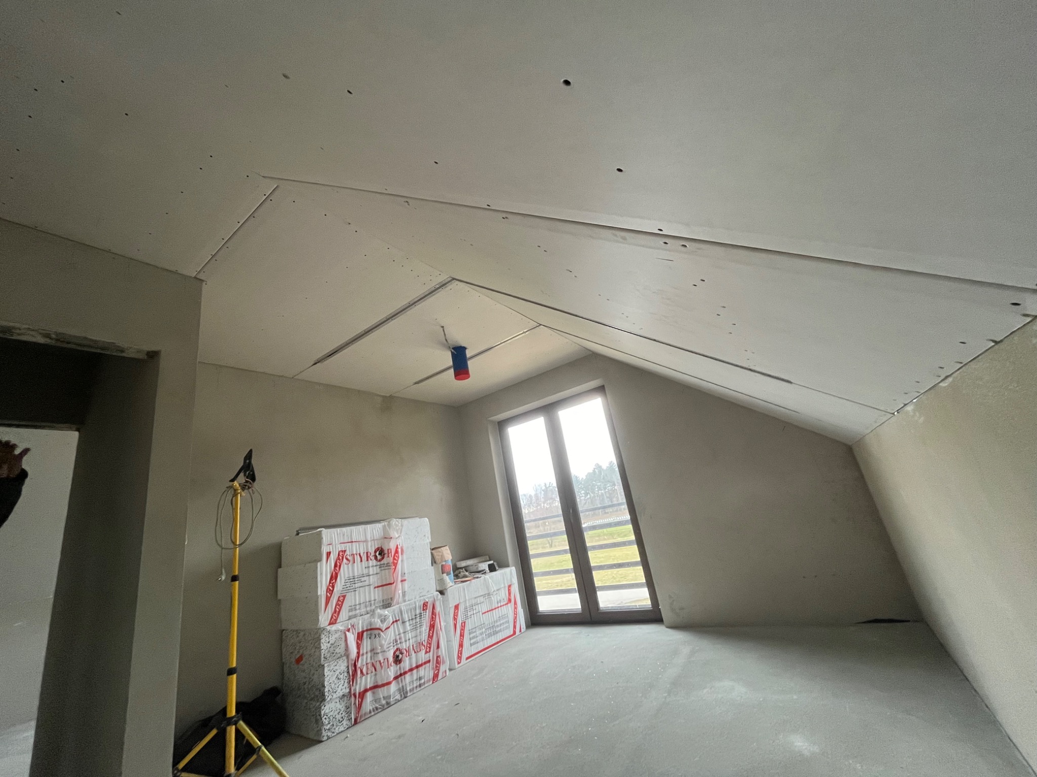 Montaż płyt na poddaszu w Łące, widoczne ocieplenie i lampa budowlana.