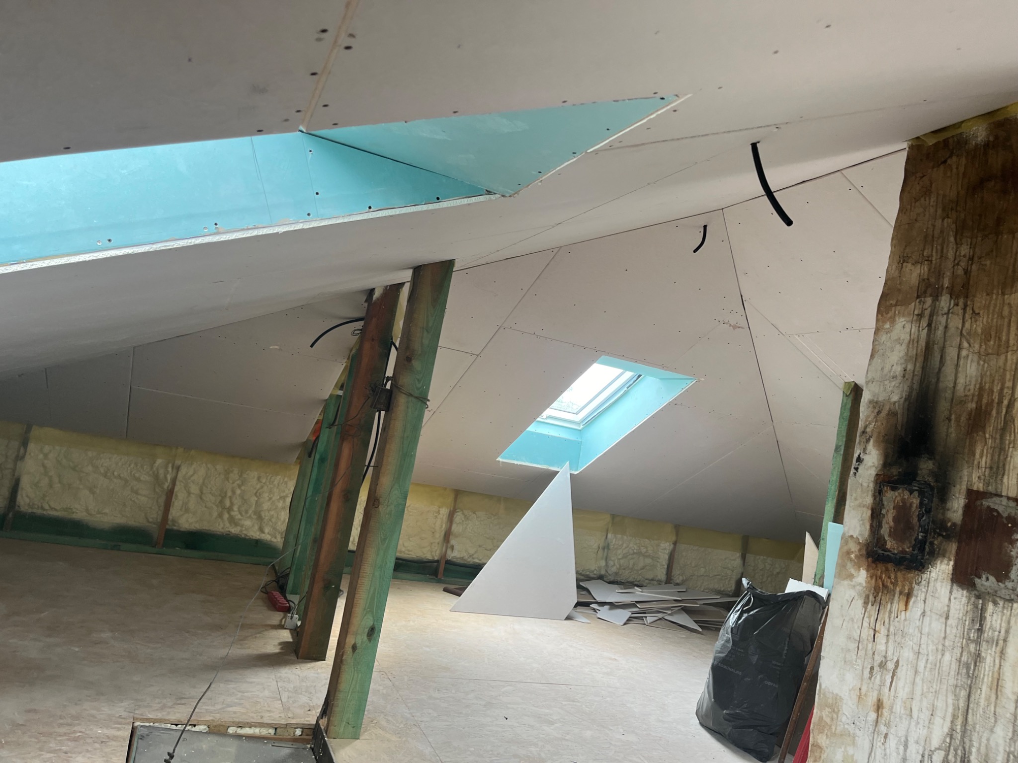 Montaż płyt w poddaszu z oknem dachowym, widoczne stelaże i izolacja piankowa, fragment nieotynkowanej ściany z zaciekami.