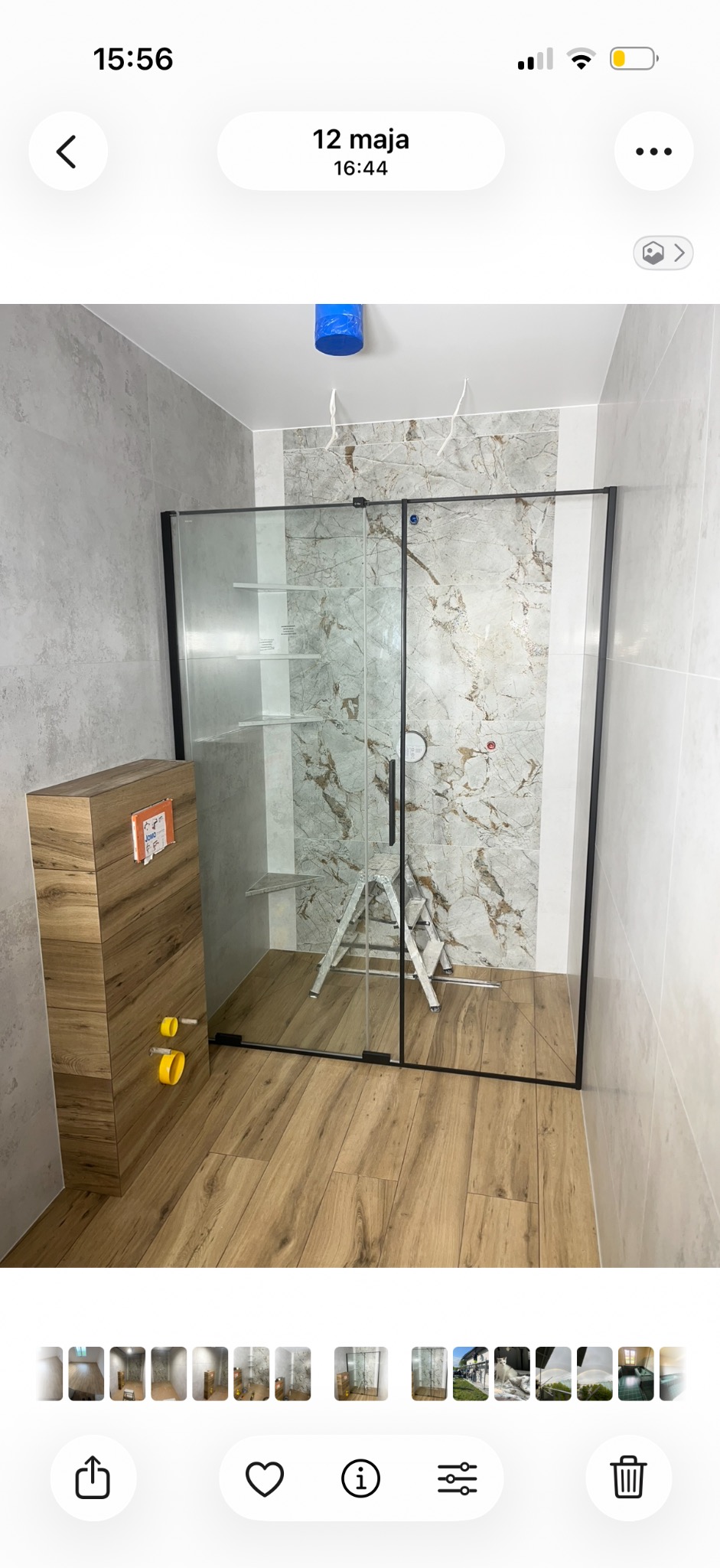 Wykończona łazienka w Łące: kabina prysznicowa z czarnymi profilami, drewnopodobne płytki podłogowe, zabudowa WC z drewnianym frontem i marmurowe płytki ścienne.