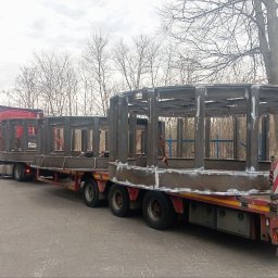 MST PROFI SPÓŁKA Z OGRANICZONĄ ODPOWIEDZIALNOŚCIĄ - Transport dwóch metalowych konstrukcji o okrągłym kształcie na naczepie ciężarówki. Widoczne spawy i surowy metal. Tablica ostrzegawcza na tyle naczepy.