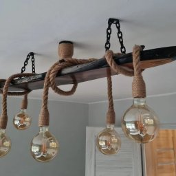 Grzegorz Lewandowski GL Timber wyroby z drewna, usługi stolarskie, meble - Lampa wisząca w stylu rustykalnym z drewnianej belki i grubego sznura, z żarówkami Edisona, mocowana do sufitu za pomocą czarnych łańcuchów.