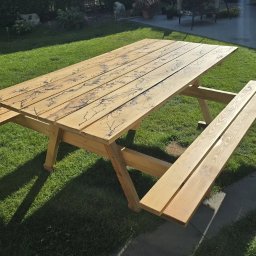 Grzegorz Lewandowski GL Timber wyroby z drewna, usługi stolarskie, meble - Drewniany stół piknikowy z ławkami, zdobiony wzorem przypominającym rozgałęzienia piorunów, ustawiony na trawniku w ogrodzie.