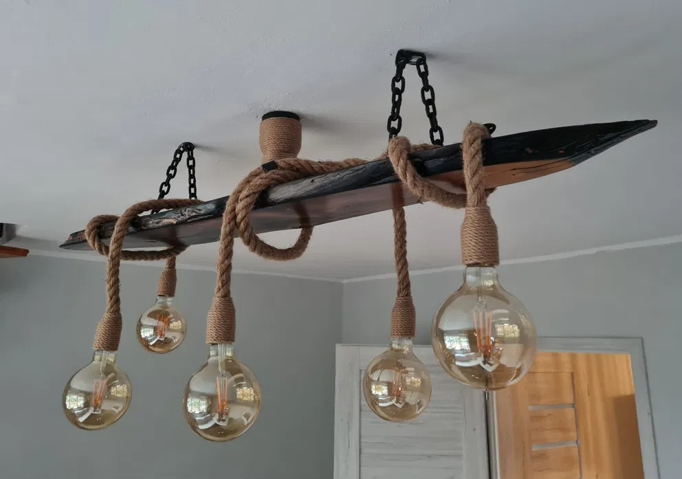 Lampa wisząca w stylu rustykalnym z drewnianej belki i grubego sznura, z żarówkami Edisona, mocowana do sufitu za pomocą czarnych łańcuchów.