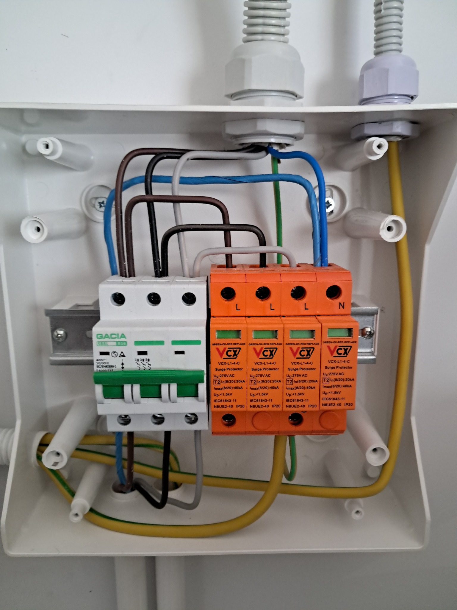 Rozdzielnica elektryczna z zabezpieczeniami przepięciowymi i wyłącznikiem różnicowoprądowym, widoczne przewody w różnych kolorach oraz oznaczenia na urządzeniach.