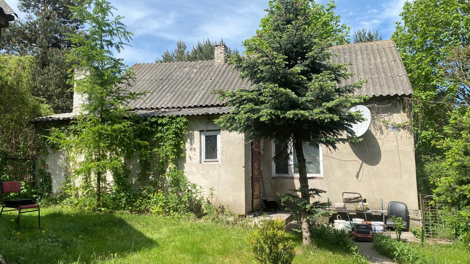 Dom jednorodzinny z szarym, falistym dachem, porośnięty zielenią, z anteną satelitarną na elewacji