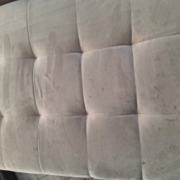 Czyścioch Usługi Sprzątające - Widok z góry na beżowy, tapicerowany puf z widocznymi plamami i zabrudzeniami, ukazujący potrzebę profesjonalnego czyszczenia tapicerki meblowej.