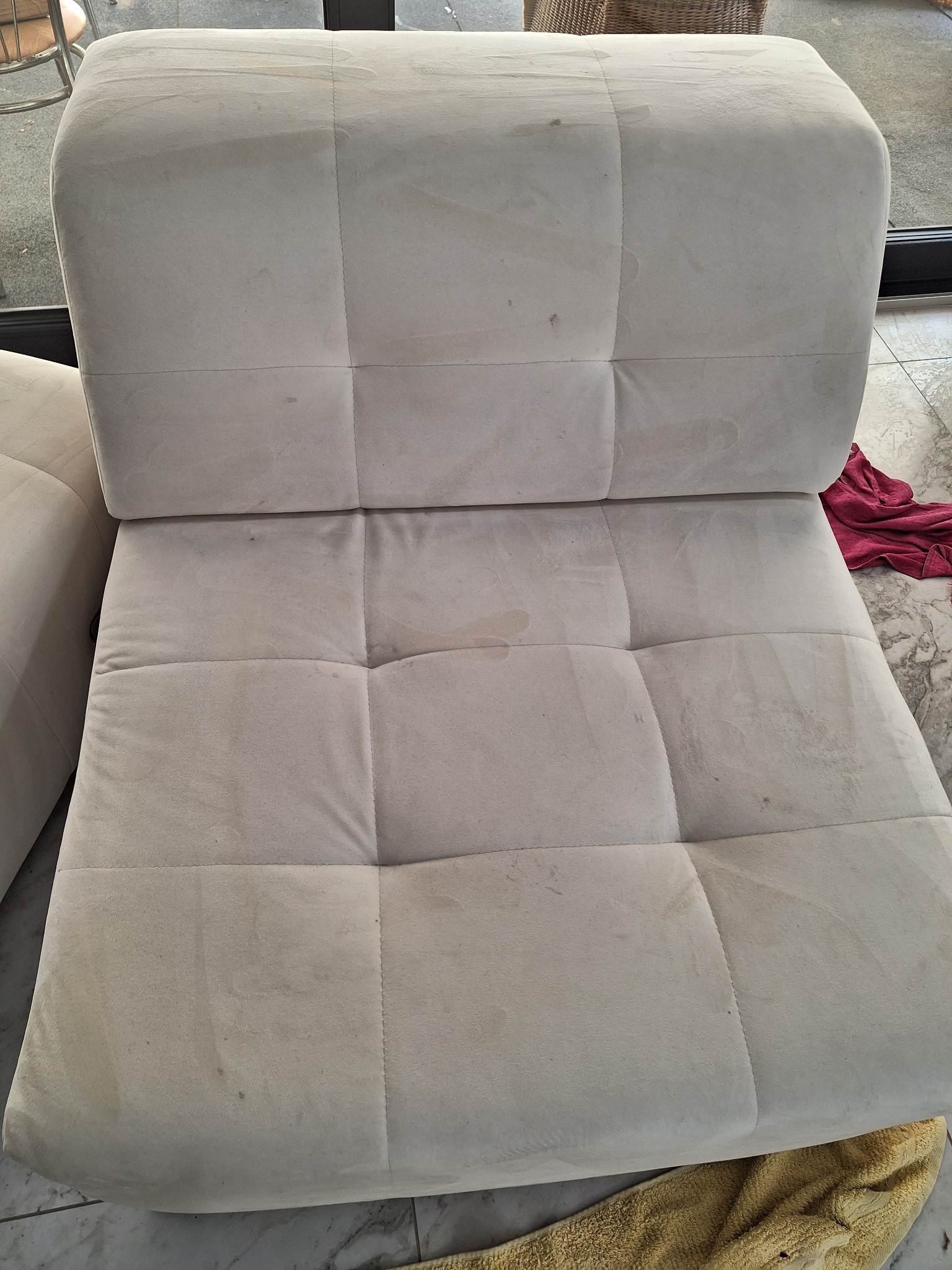 Tapicerowany, kremowy fotel modułowy z widocznymi plamami na siedzisku i oparciu, czekający na pranie. W tle fragment podłogi z marmurowym wzorem.