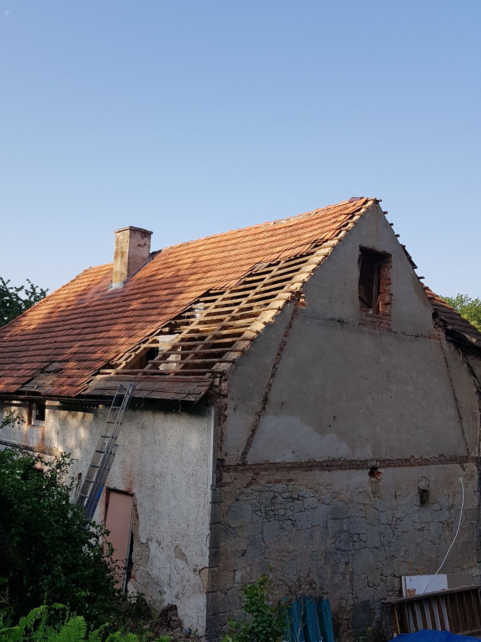 Częściowo zdjęty dach z czerwonej dachówki na starym domu w Lwówku Śląskim. Widoczne krokwie i komin. Przystawiona drabina.