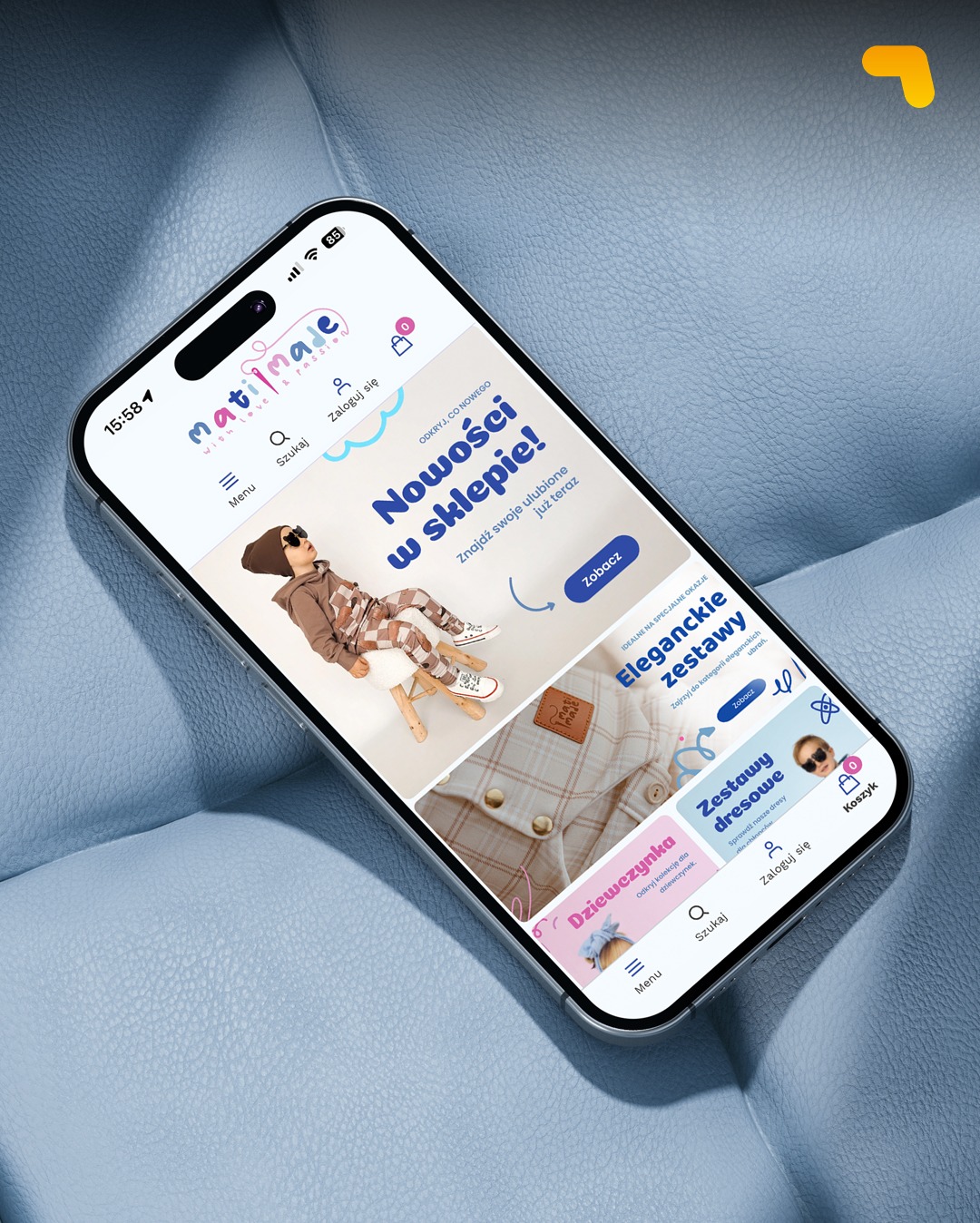 Smartfon wyświetla stronę sklepu internetowego z odzieżą dziecięcą na tle niebieskiej, teksturowanej powierzchni. Widoczne menu, kategorie produktów i logo sklepu.