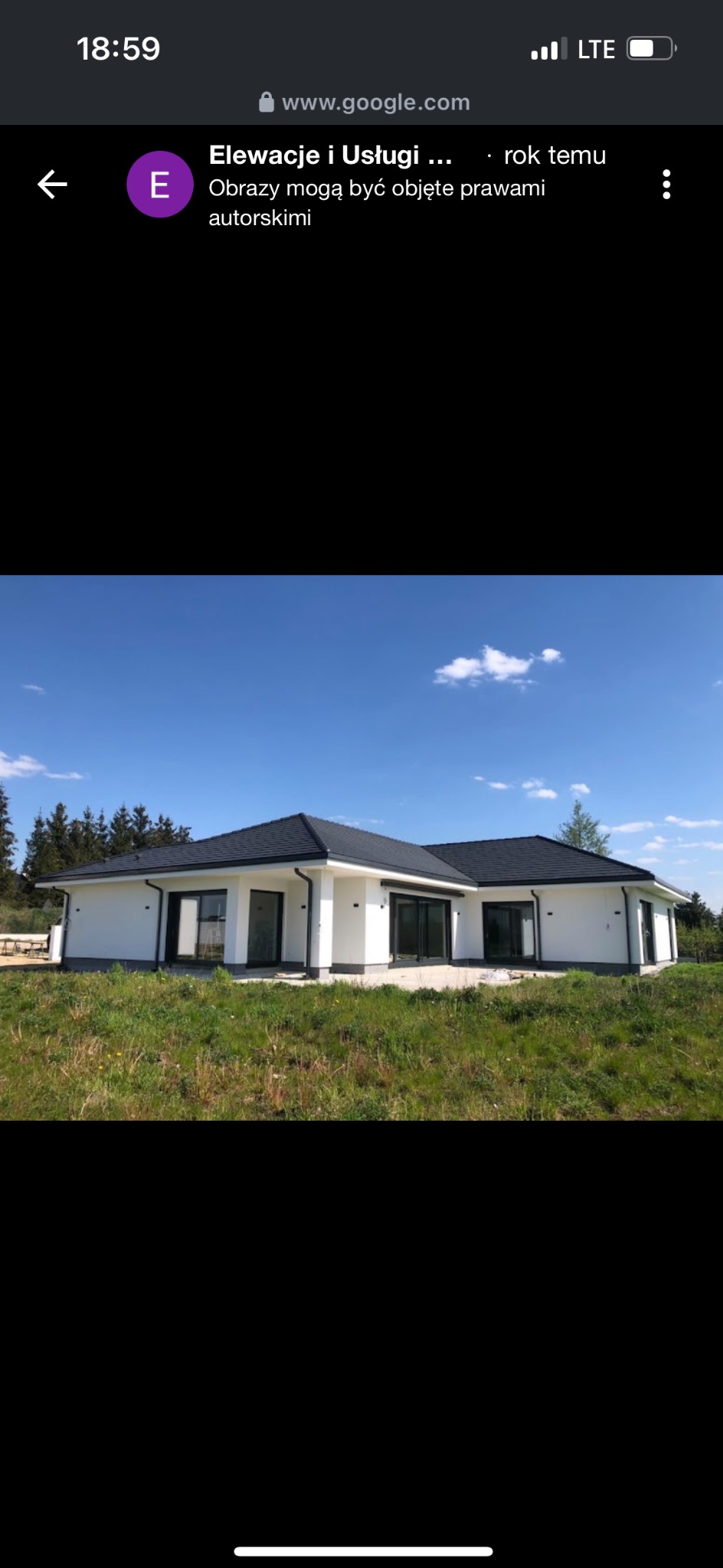 Nowoczesny, parterowy dom z białą elewacją i ciemnym dachem na tle zielonego trawnika i błękitnego nieba.