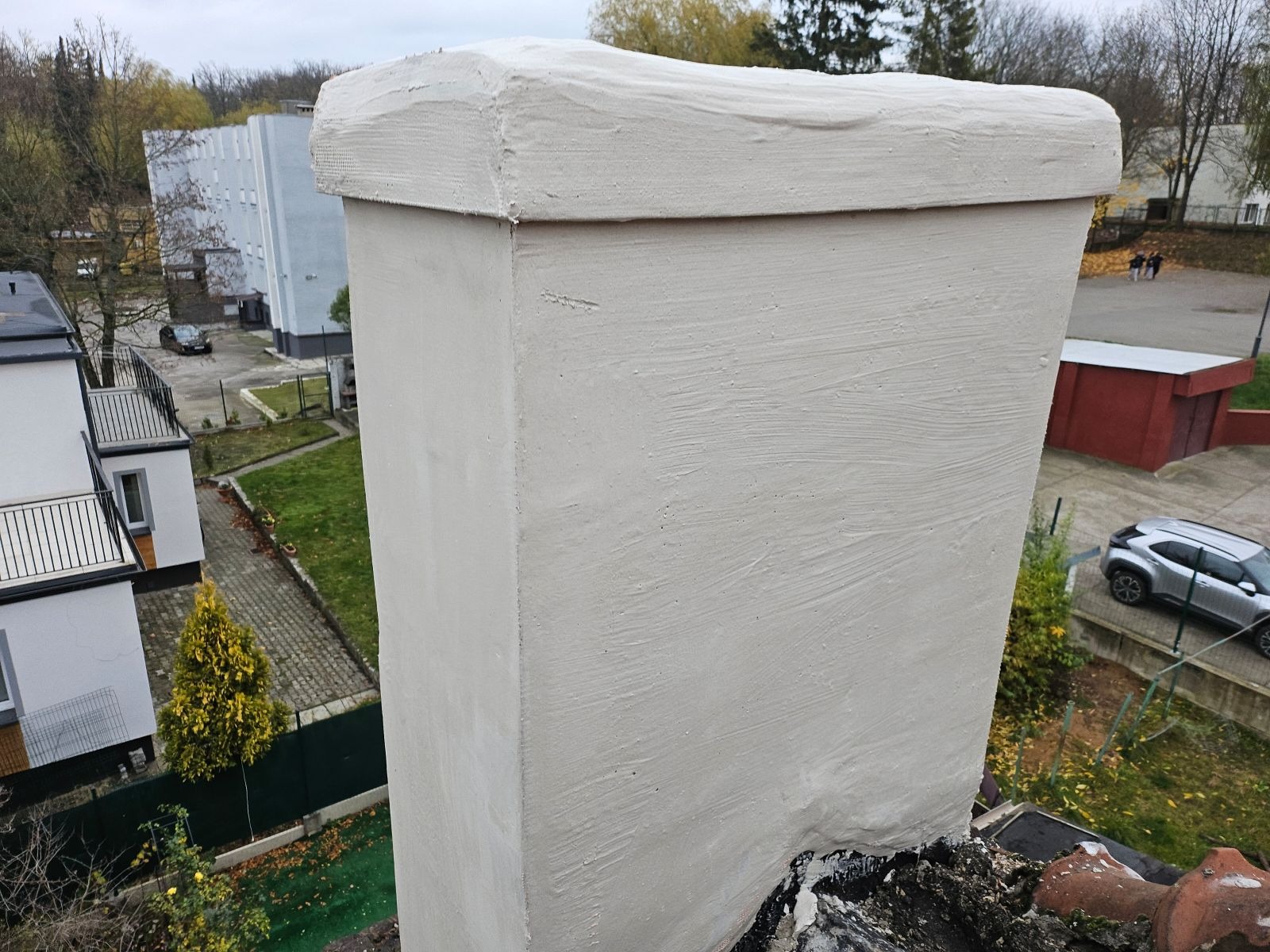 Otynkowany komin z widoczną fakturą świeżego tynku na tle budynków mieszkalnych i zieleni