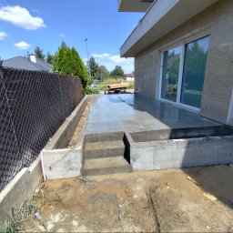 DarBet - Świeżo wylany, mokry betonowy taras z trzema stopniami, widok z boku, z widoczną siatką ogrodzeniową i przygotowanym podłożem.