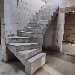 DarBet - Surowe, betonowe schody spiralne w trakcie budowy, widoczne ściany z bloczków betonowych i surowy betonowy strop, brak wykończenia.