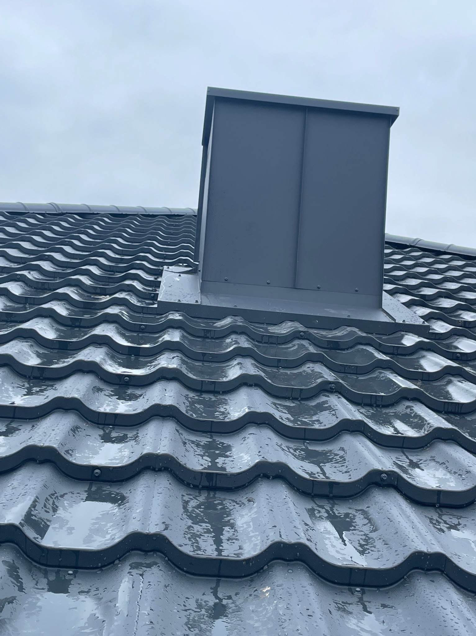 Szary, metalowy dach z kominem w Obornikach, pokryty kroplami deszczu, widok z dołu.