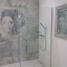 Przemysław Rolnik - Nowoczesna kabina prysznicowa z szarymi płytkami imitującymi beton, zdobiona portretem kobiety, z odpływem liniowym i lustrem z odbiciem tej samej twarzy.