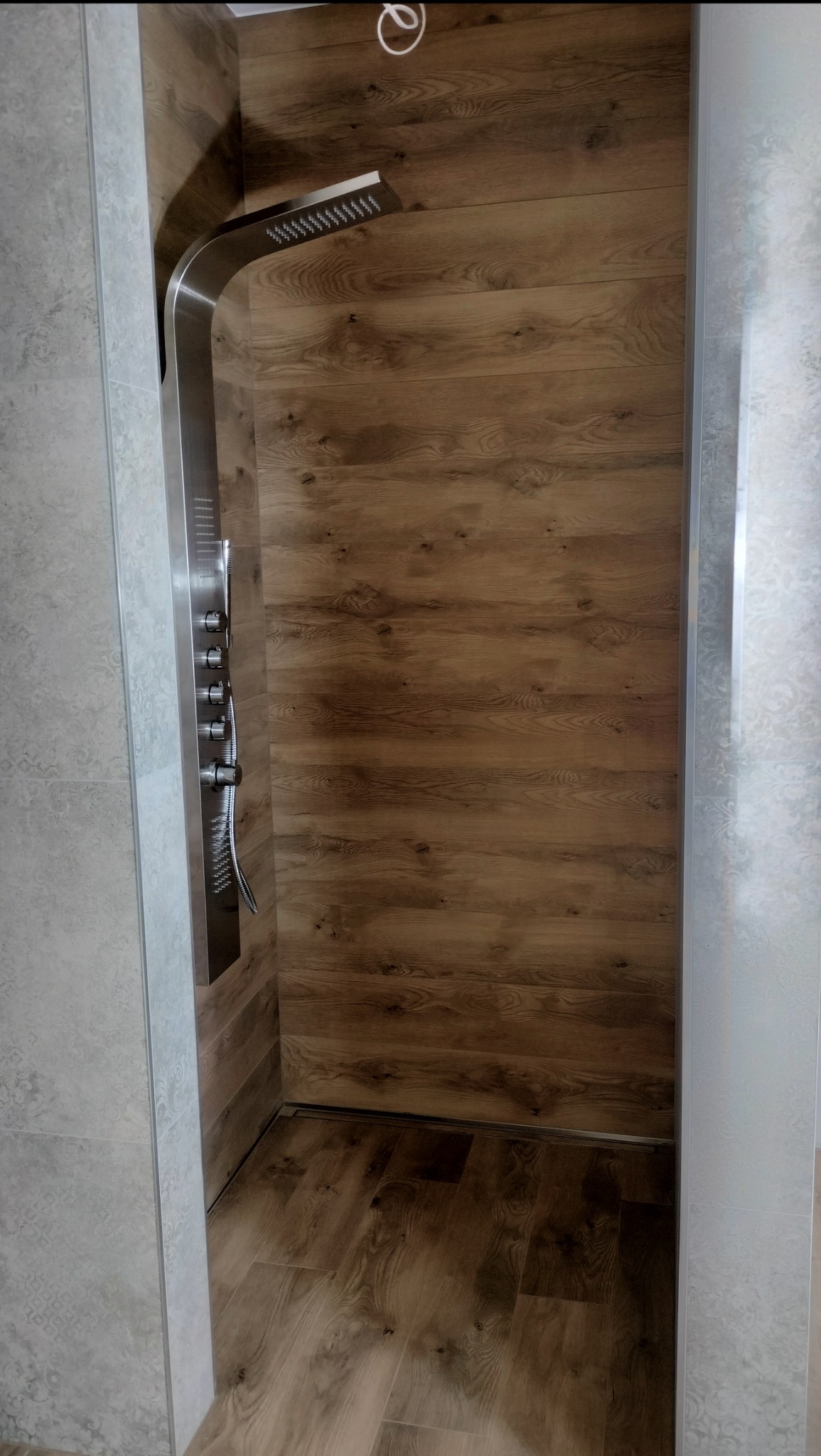 Nowoczesna kabina prysznicowa z panelem natryskowym ze stali nierdzewnej i drewnopodobną okładziną ścienną i podłogową, zrealizowana w Żarnowie.