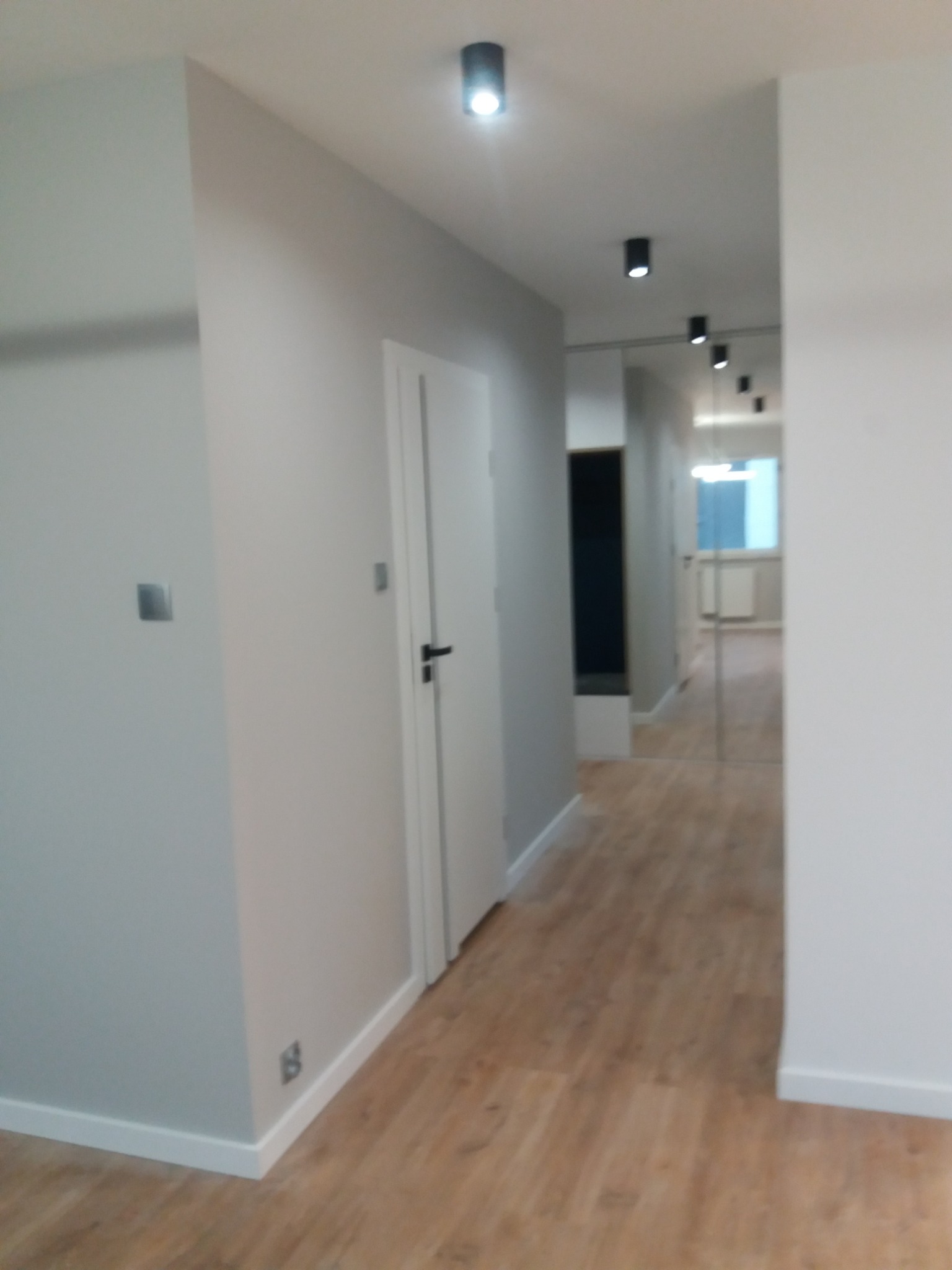 Nowoczesny korytarz w odcieniach szarości z drewnianą podłogą, oświetleniem punktowym i minimalistycznymi drzwiami.