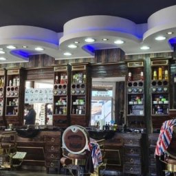 Glazurowe Wybrzeże - Wnętrze luksusowego salonu fryzjerskiego w stylu vintage z ciemnego drewna, z oświetleniem LED, trzema stanowiskami pracy i dwoma fryzjerami obsługującymi klientów.