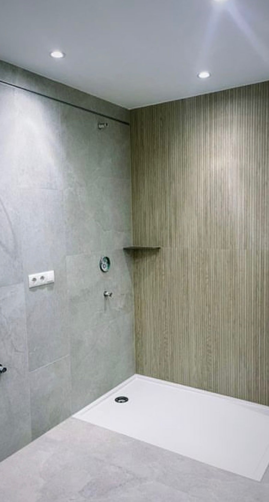 Nowoczesna kabina prysznicowa z szarymi płytkami imitującymi kamień, drewnopodobnymi panelami ściennymi, białą brodzikiem i minimalistyczną półką.