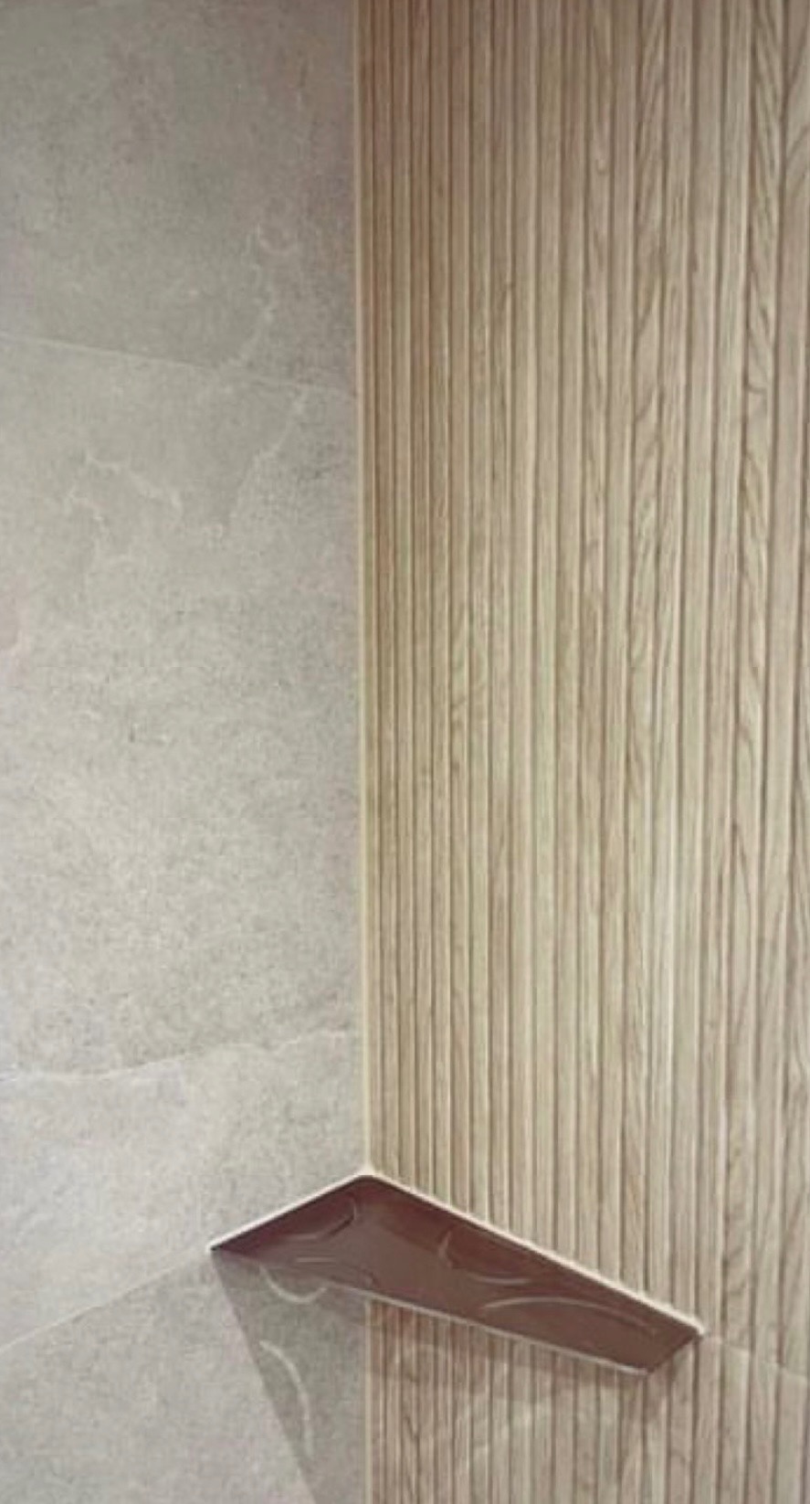 Fragment wykończonej łazienki z płytkami imitującymi drewno na ścianie i półką w rogu, wykończoną brązowymi płytkami.