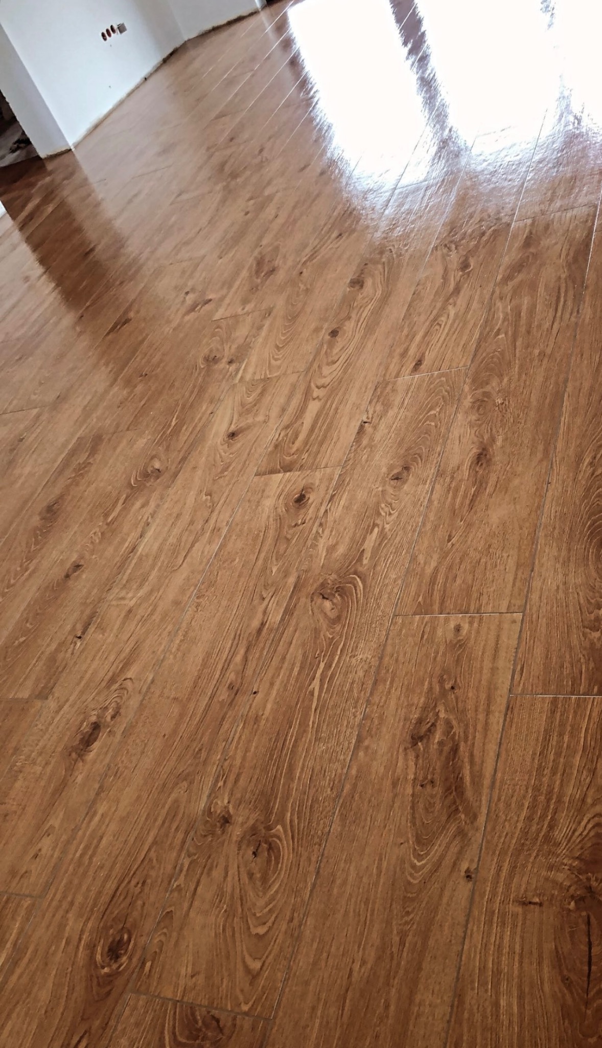 Świeżo położona, błyszcząca podłoga z paneli imitujących drewno dębowe, widoczne delikatne refleksy świetlne.