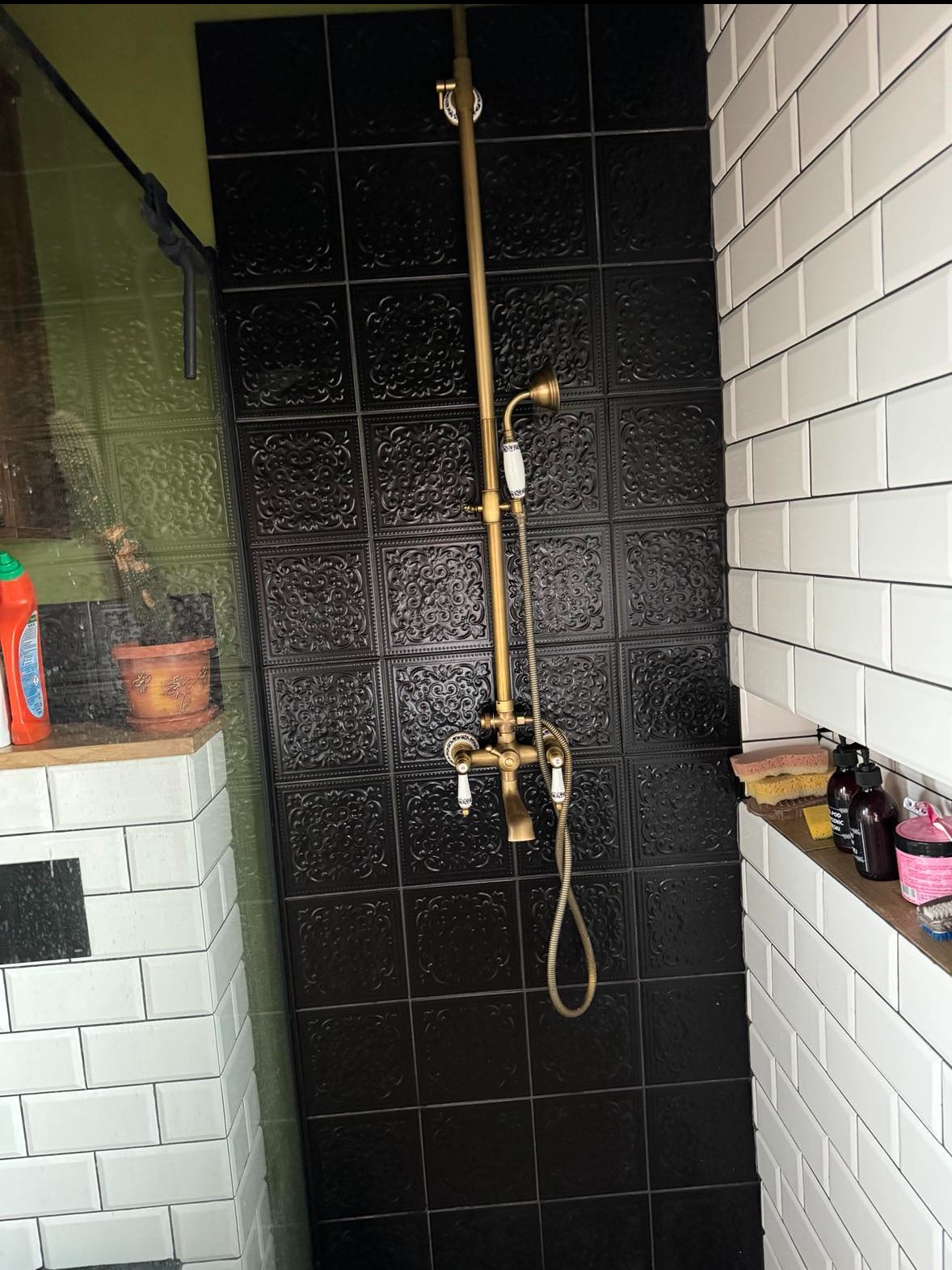 Łazienka z czarnymi płytkami dekoracyjnymi i złotą armaturą retro, białe kafelki typu metro na ścianach, widoczna półka z kosmetykami i akcesoriami.