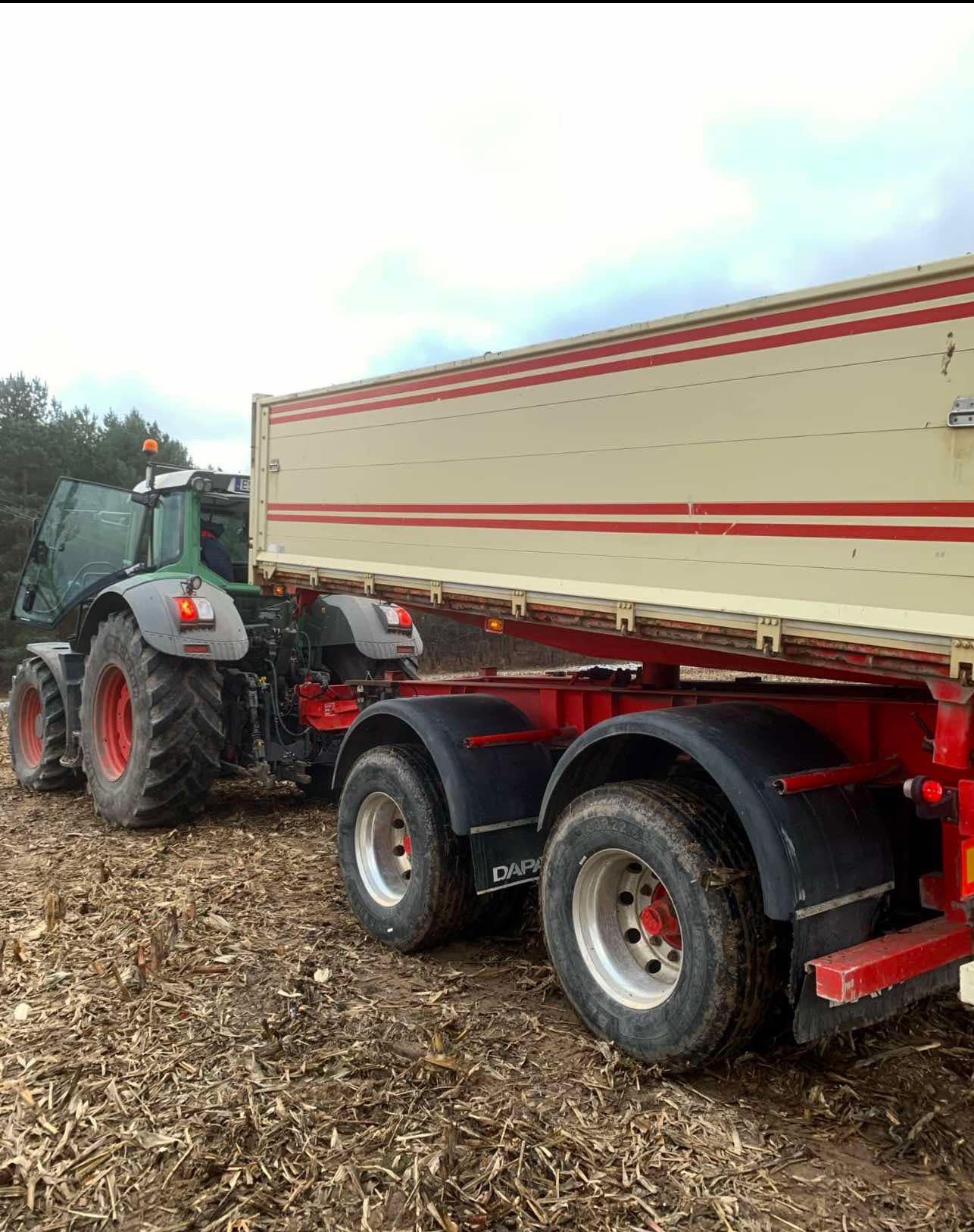 Ciężki traktor z otwartą maską i przyczepą na polu z resztkami po zbiorach, widoczne duże koła i błotniki przyczepy.