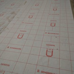 Best Tilers Group Kamil Pieczajka - Przygotowanie podłoża pod płytki z użyciem maty izolacyjnej z siatką w Lublinie, widoczny worek zaprawy.