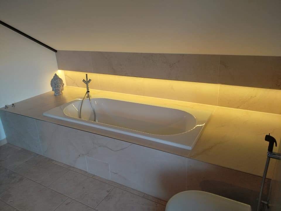 Wanna obudowana płytkami imitującymi marmur, podświetlana od góry ciepłym światłem LED, z dekoracyjną figurką Buddy i baterią w stylu retro.