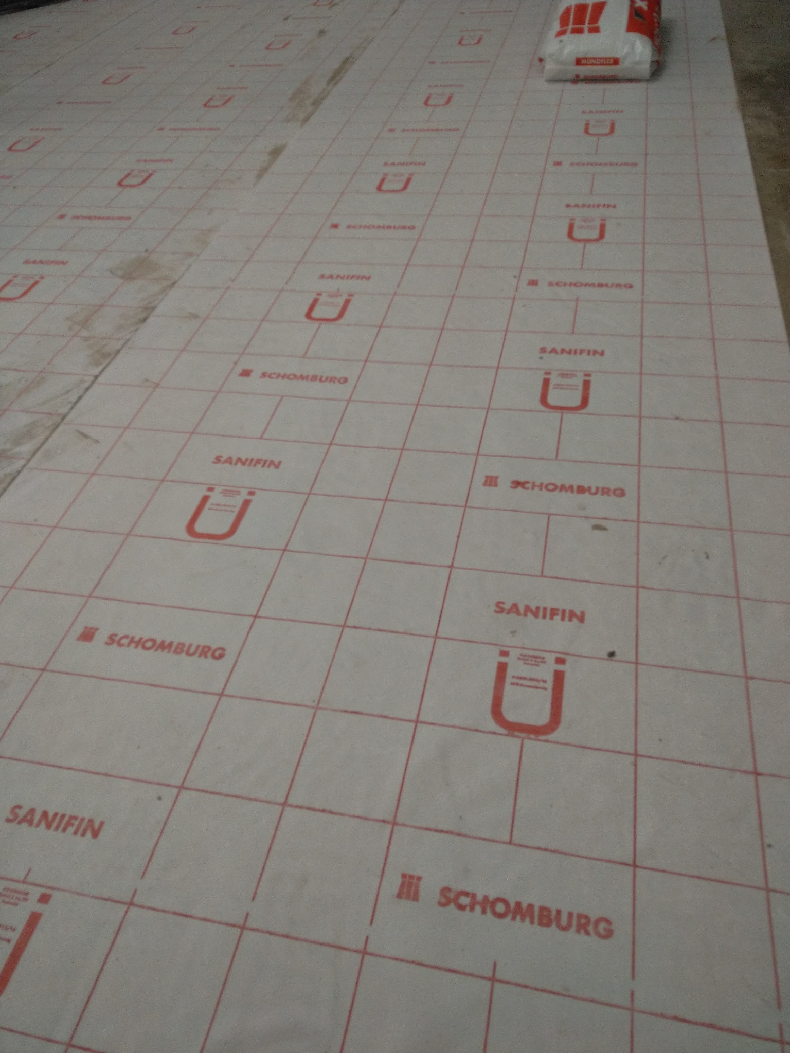 Przygotowanie podłoża pod płytki z użyciem maty izolacyjnej z siatką w Lublinie, widoczny worek zaprawy.