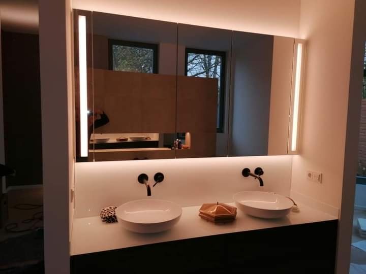 Nowoczesna łazienka z podwójną umywalką nablatową, czarną armaturą i podświetlanym lustrem z szafkami, odbijającym widok przez okno.