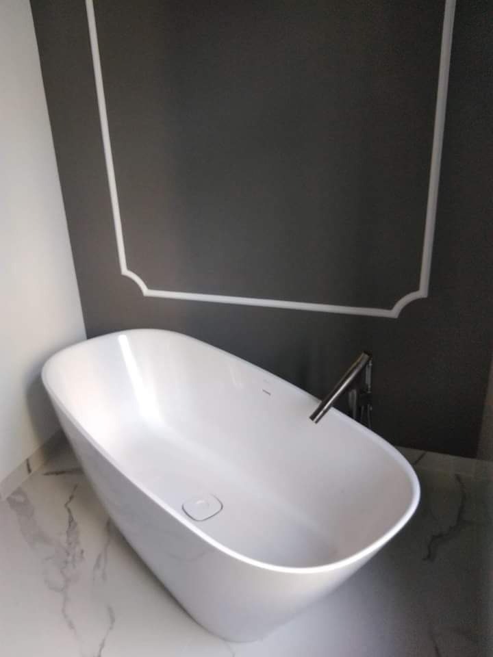 Wolnostojąca wanna w nowoczesnej łazience z szarymi ścianami, białą sztukaterią i marmurową podłogą.