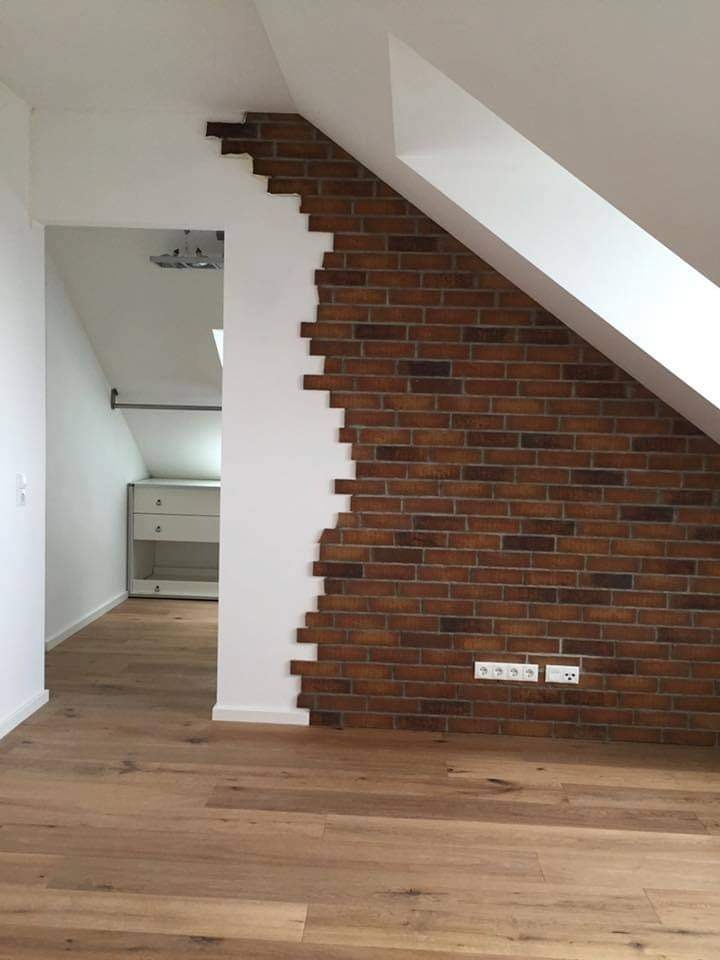 Ściana z cegły klinkierowej w pokoju na poddaszu, z widoczną instalacją elektryczną i drewnianą podłogą, częściowo pomalowana na biało, z nieregularnym brzegiem.