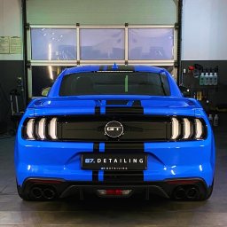 RB MOTORS RAFAŁ BOGACKI - Błękitny Ford Mustang GT z czarnymi pasami, widok z tyłu, po detailingu w warsztacie, z widocznym logo firmy na tablicy rejestracyjnej.