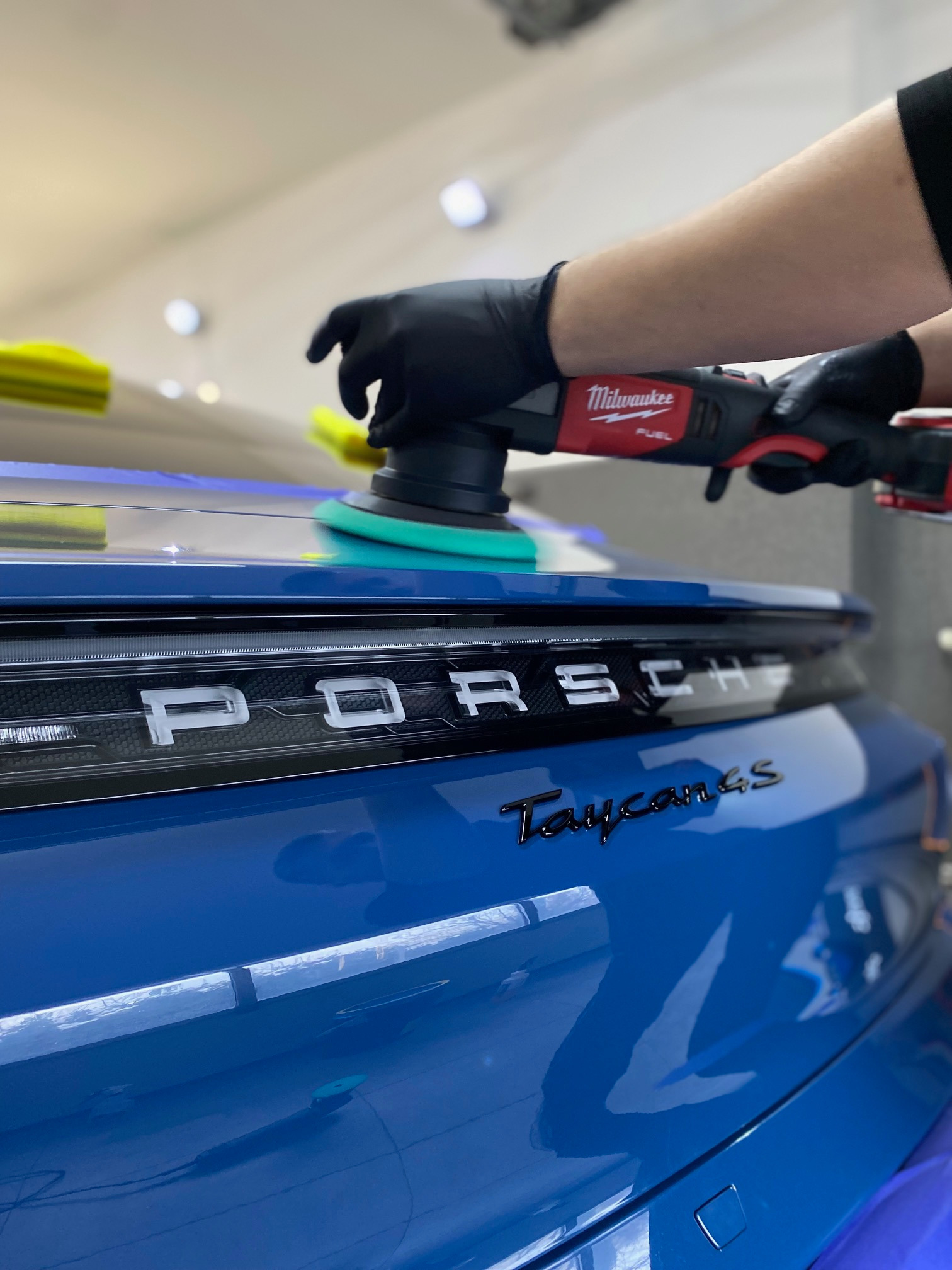 Detailing lakieru niebieskiego Porsche Taycan 4S za pomocą polerki Milwaukee Fuel z zielonym padem polerskim, widoczne odbicia światła na lakierze.