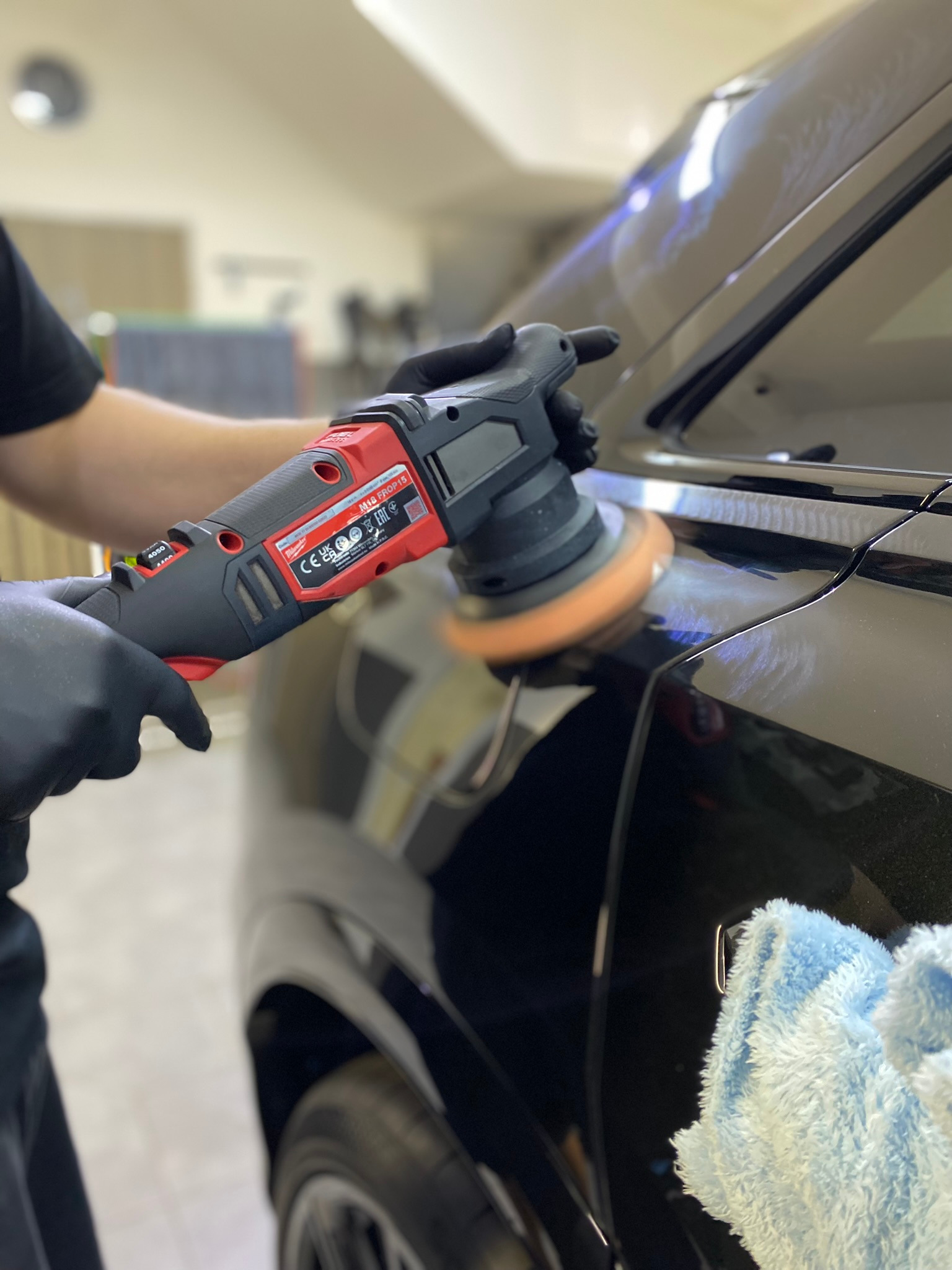 Detailing czarnego samochodu: polerowanie lakieru za pomocą polerki elektrycznej Milwaukee M18 FROP15, widoczny efekt hologramów na lakierze przed polerowaniem.