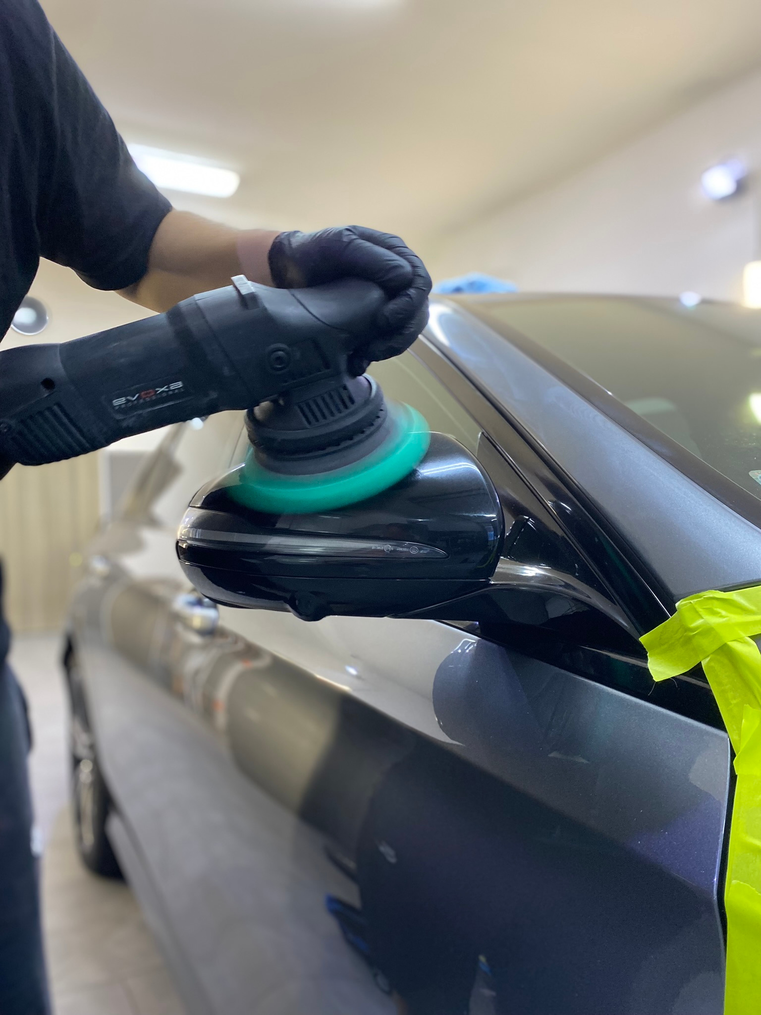 Polerowanie lusterka bocznego samochodu za pomocą polerki elektrycznej, widoczne taśmy zabezpieczające lakier.